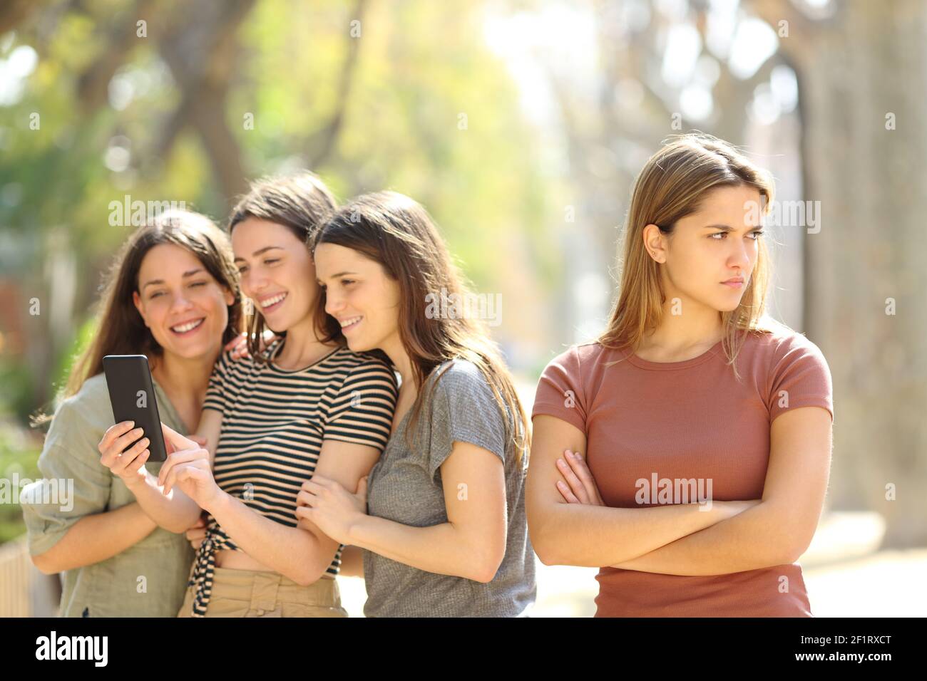 Donna arrabbiata ignorata dai suoi amici felici che sono controllo del contenuto dello smartphone in strada Foto Stock