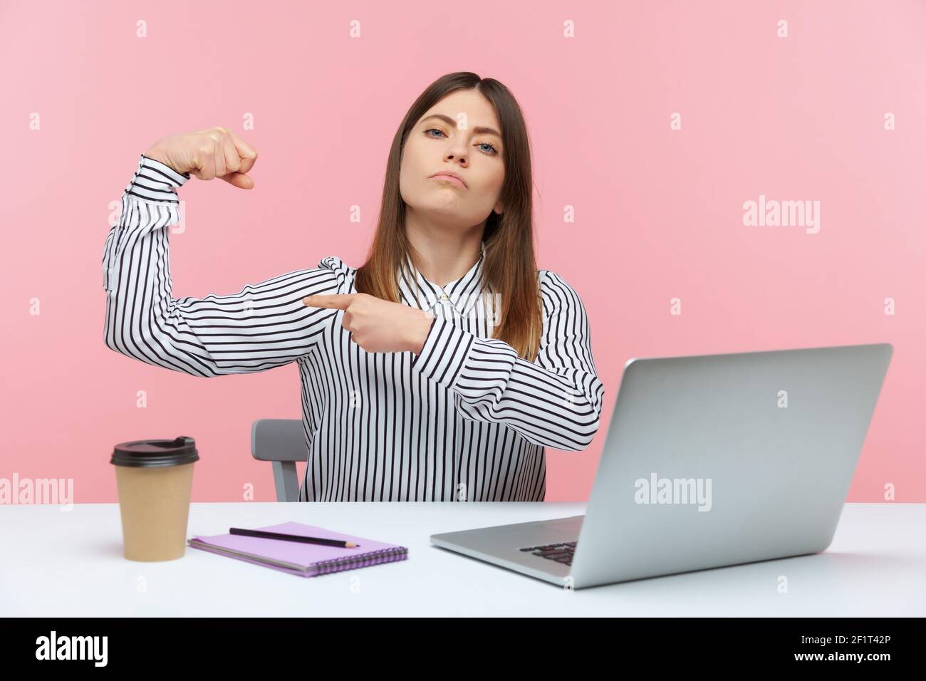 Donna di affari forte bossy che mostra i suoi muscoli seriamente guardando la macchina fotografica con espressione sicura, sentendosi libero ed indipendente nella posizione principale. Foto Stock
