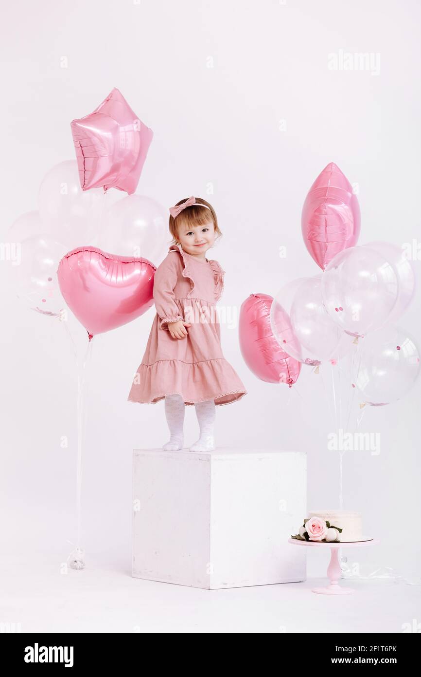 la bambina di compleanno di 2 anni in abito rosa. torta bianca con candele  e rose. Decorazioni di compleanno con palloncini bianchi e rosa e con Foto  stock - Alamy