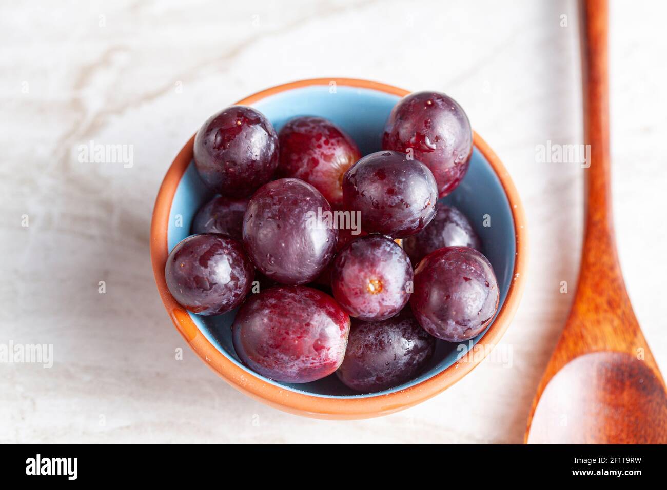 Una semplice immagine di una ciotola di porcellana o di uva rossa e di un cucchiaio di legno sul piano di marmo. Un'immagine concettuale per un'alimentazione vegana e sana. Foto Stock