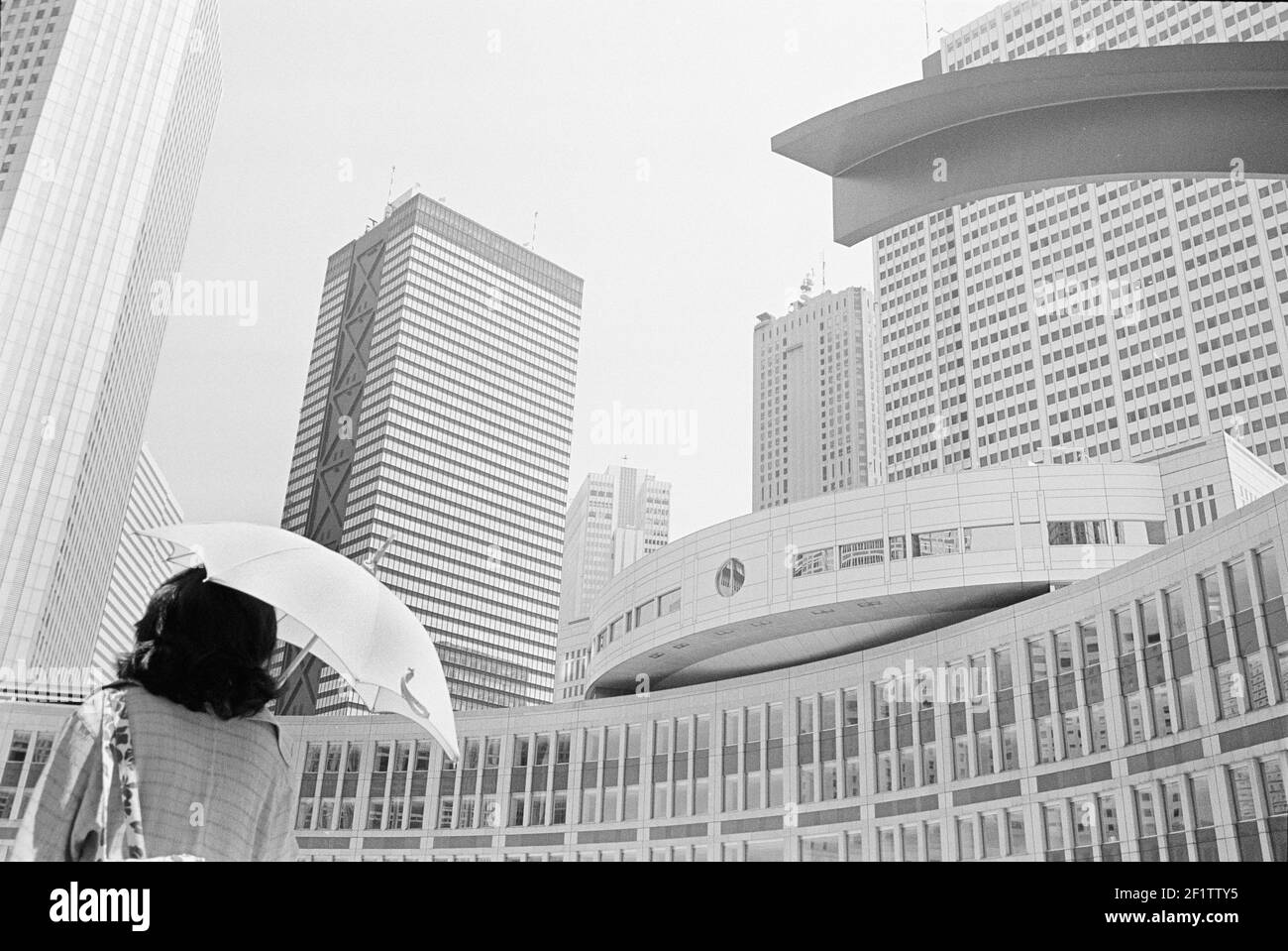 Donna con ombrello che passa attraverso la moderna architettura futuristica e gli edifici nel famoso distretto di Tokyo Nishi-Shinjuku, Giappone Foto Stock