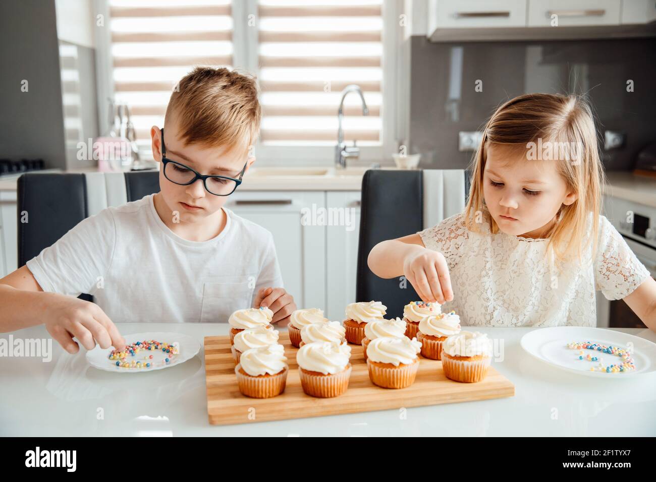 Due bambini decorano i cupcakes spruzzando le sfere di glassatura su loro Foto Stock