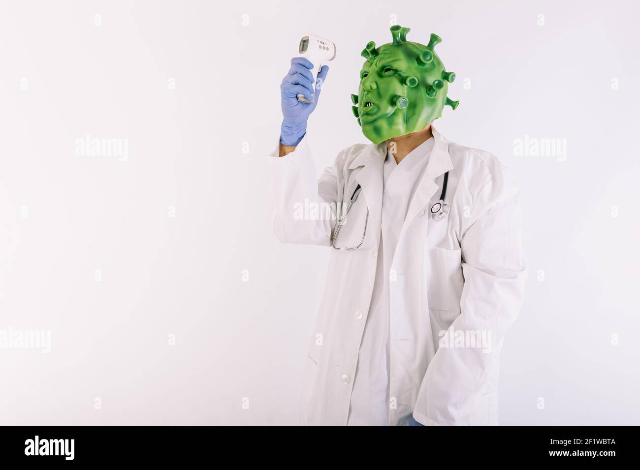 Persona vestita da coronavirus con maschera in lattice - virus covid-19, indossando un costume da medico, misurandone la temperatura con un termometro elettronico, Foto Stock