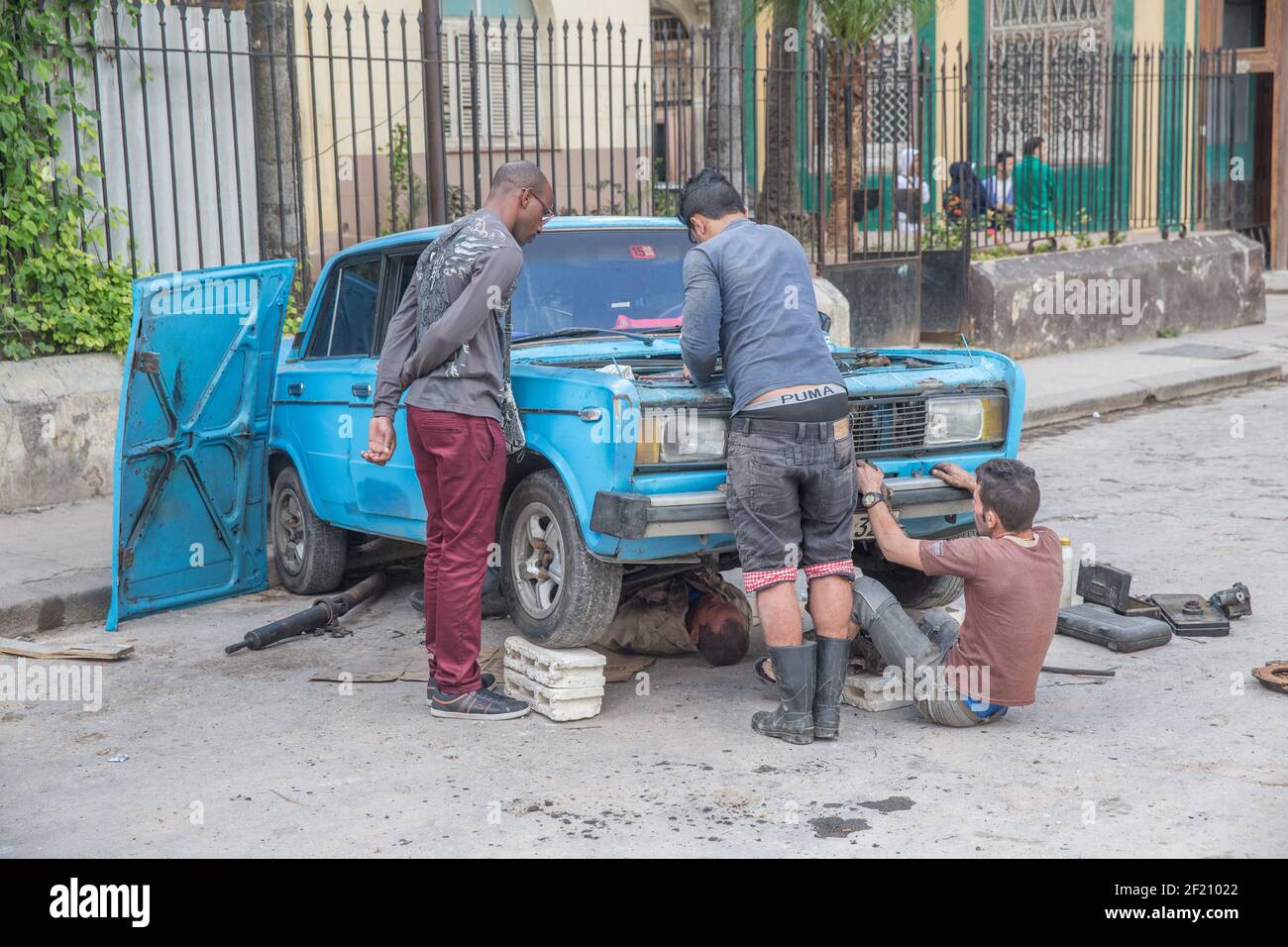 Cuba, l'Avana - uomini che riparano l'auto sui blocchetti di cinderblock nella strada Foto Stock