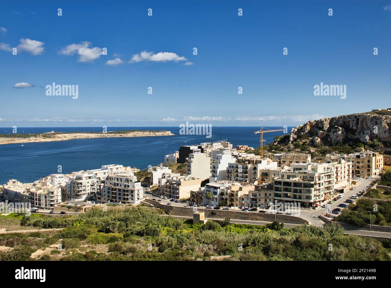 Edifici bianchi su una collina accanto all'oceano a Mellieha, Malta, in una calda e soleggiata giornata di autunno. Foto Stock