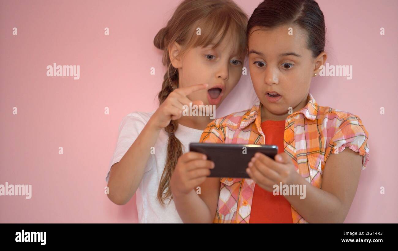 Le ragazze piccole felici con uno smartphone nelle mani comunicano a. casa con i tuoi cari utilizzando la tecnologia moderna Foto Stock