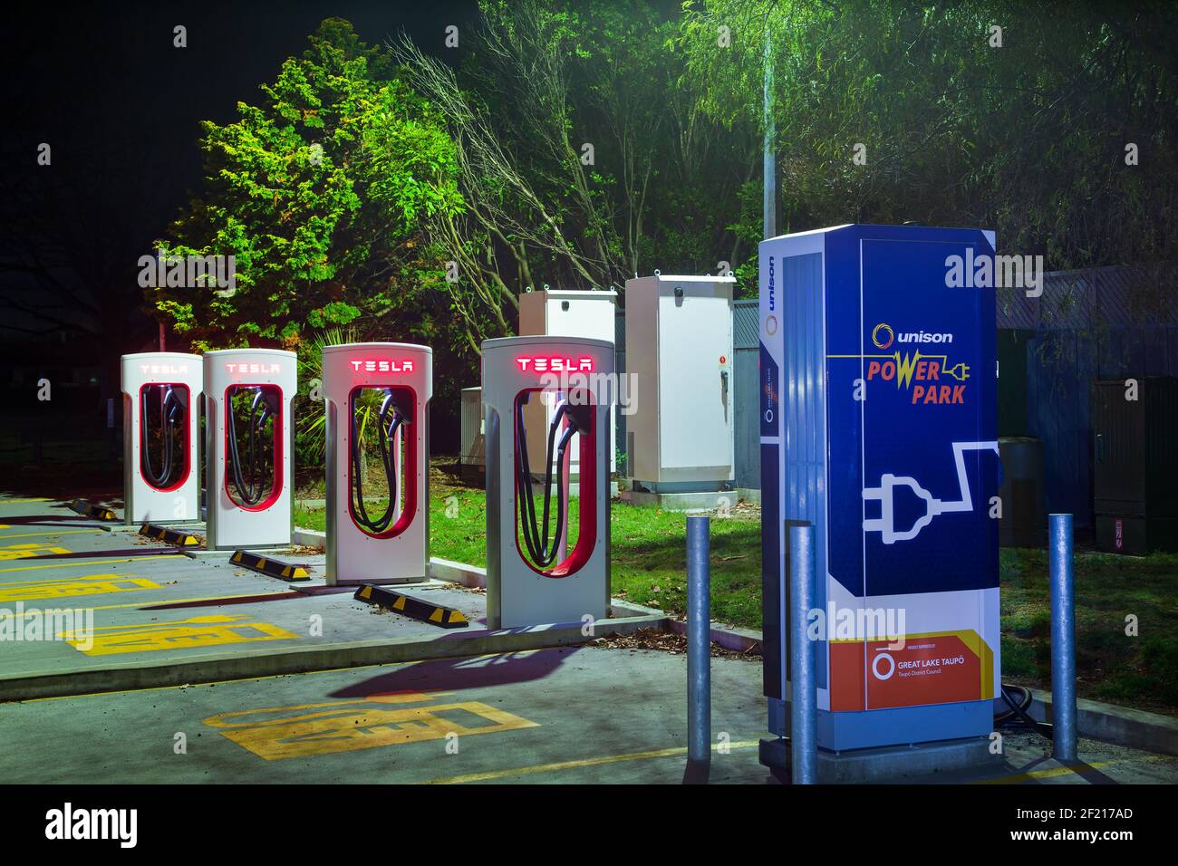 Una fila di stazioni di ricarica per veicoli elettrici di notte. La maggior parte di loro ha il logo Tesla. Taupo, Nuova Zelanda Foto Stock