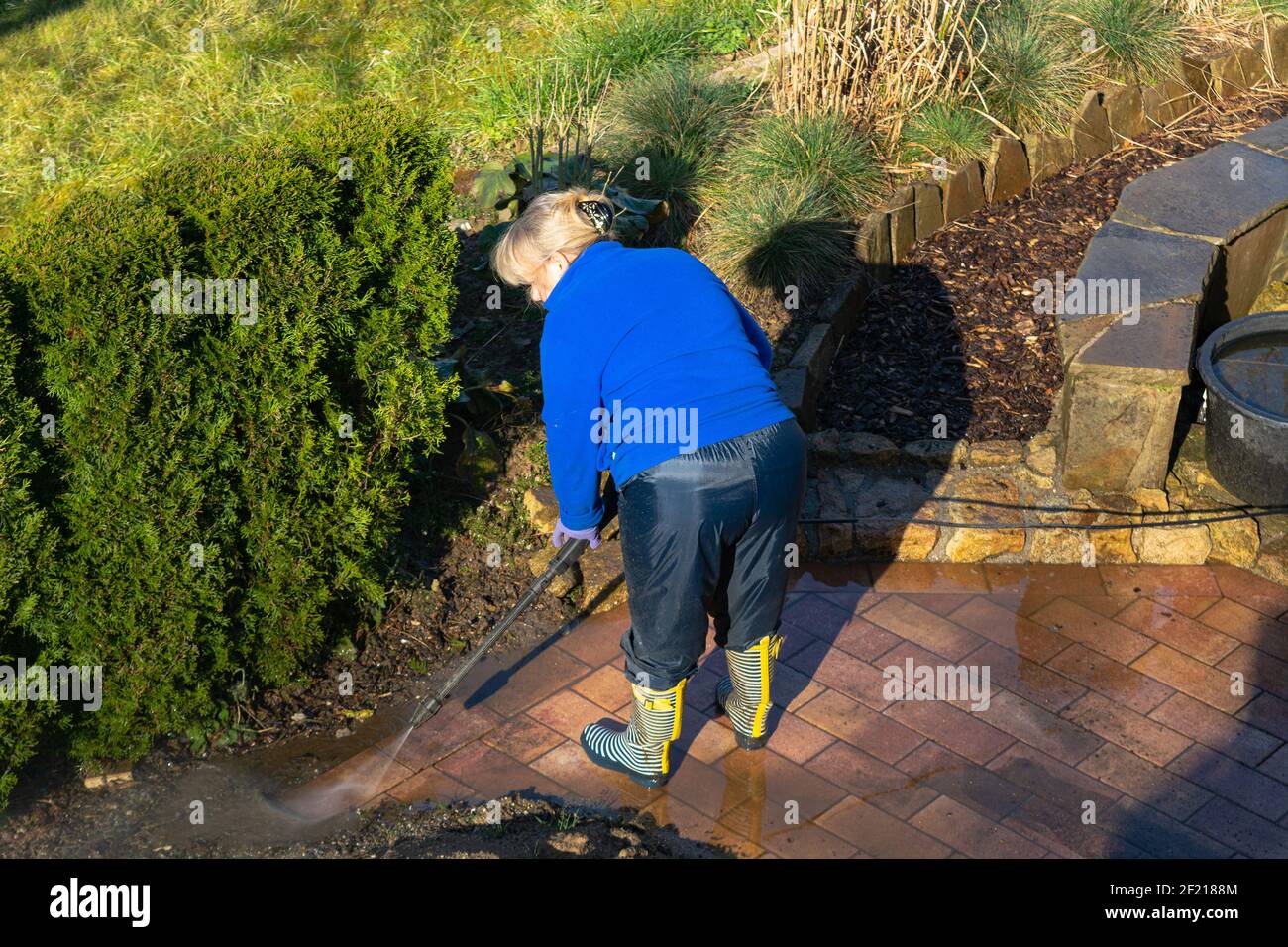 Donna che pulisce la terrazza con una lavatrice - acqua alta pulitore a pressione su superfici in legno Foto Stock