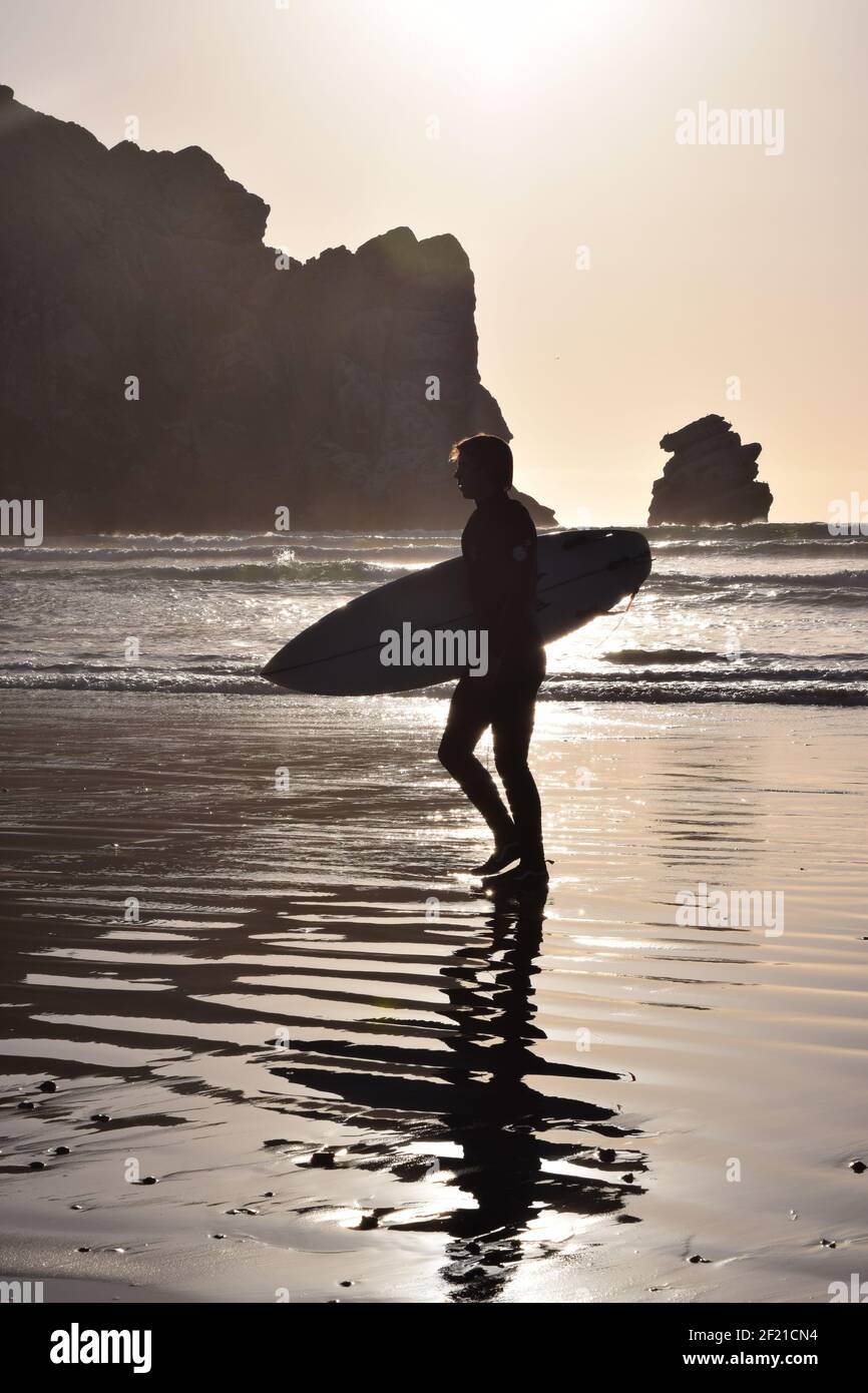 FRESNO, STATI UNITI - Mar 04, 2021: Una foto da vicino di una silhouette di un surfer maschio che tiene la sua Surfboard contro un sole soffusa e luminoso che mostra la sua r Foto Stock