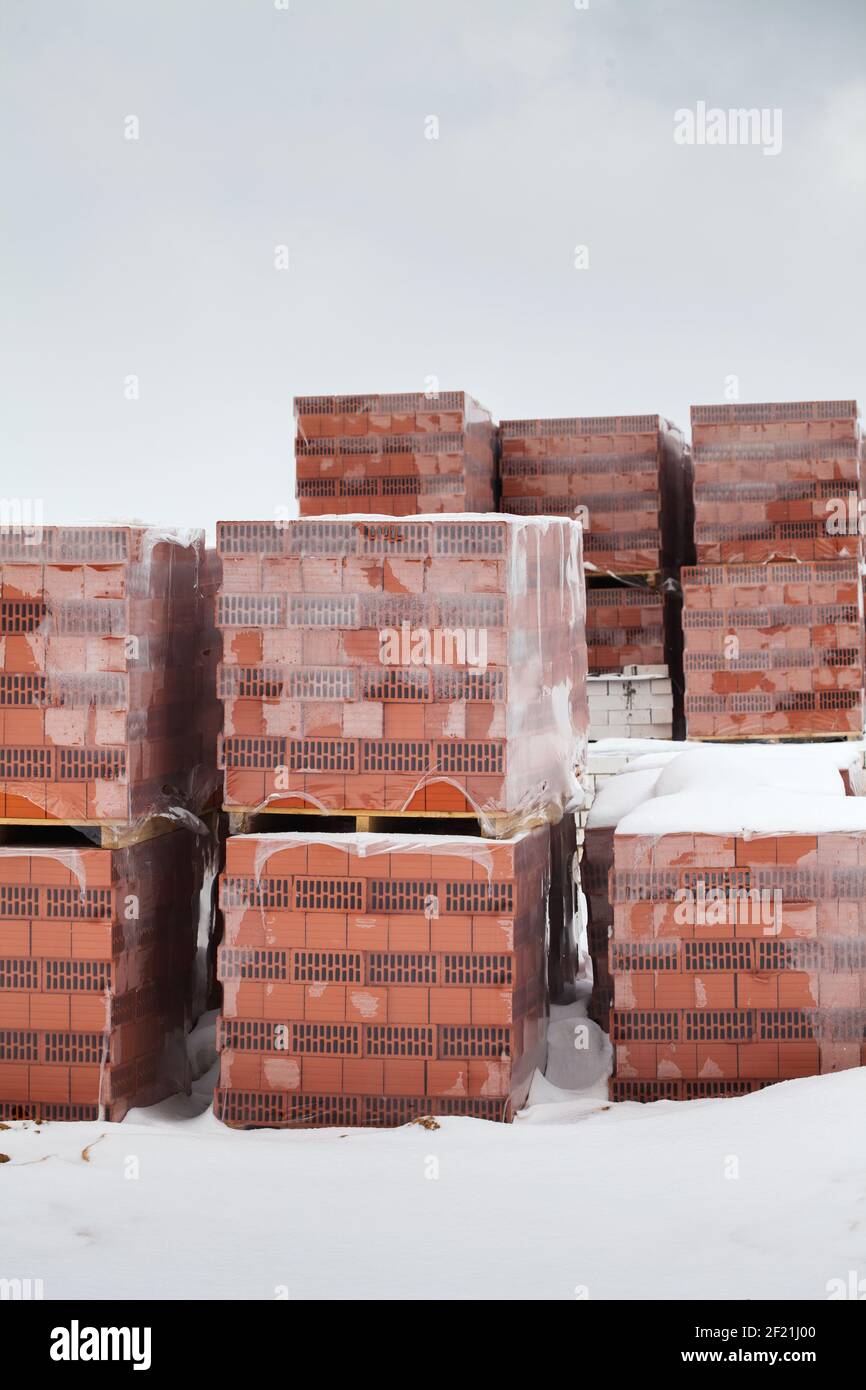 Preparazione per la costruzione di una casa, una pausa dalla costruzione per l'inverno. Pacchetti di mattoni rossi si trovano all'esterno sotto la neve Foto Stock