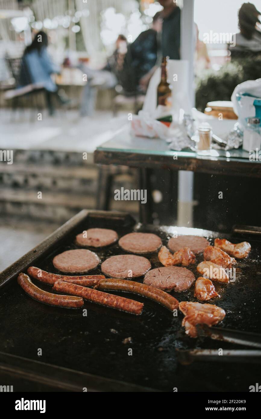 Un primo piano di un braciere oleoso con salsicce, cotolette e pollo fritto in cucina su uno sfondo sfocato Foto Stock