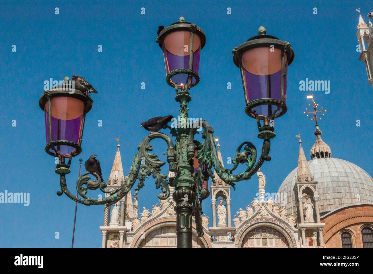 Vecchia lanterna a 4 fiamme splendidamente decorata di fronte alla cattedrale di Venezia. I piccioni si siedono sulla lanterna Foto Stock