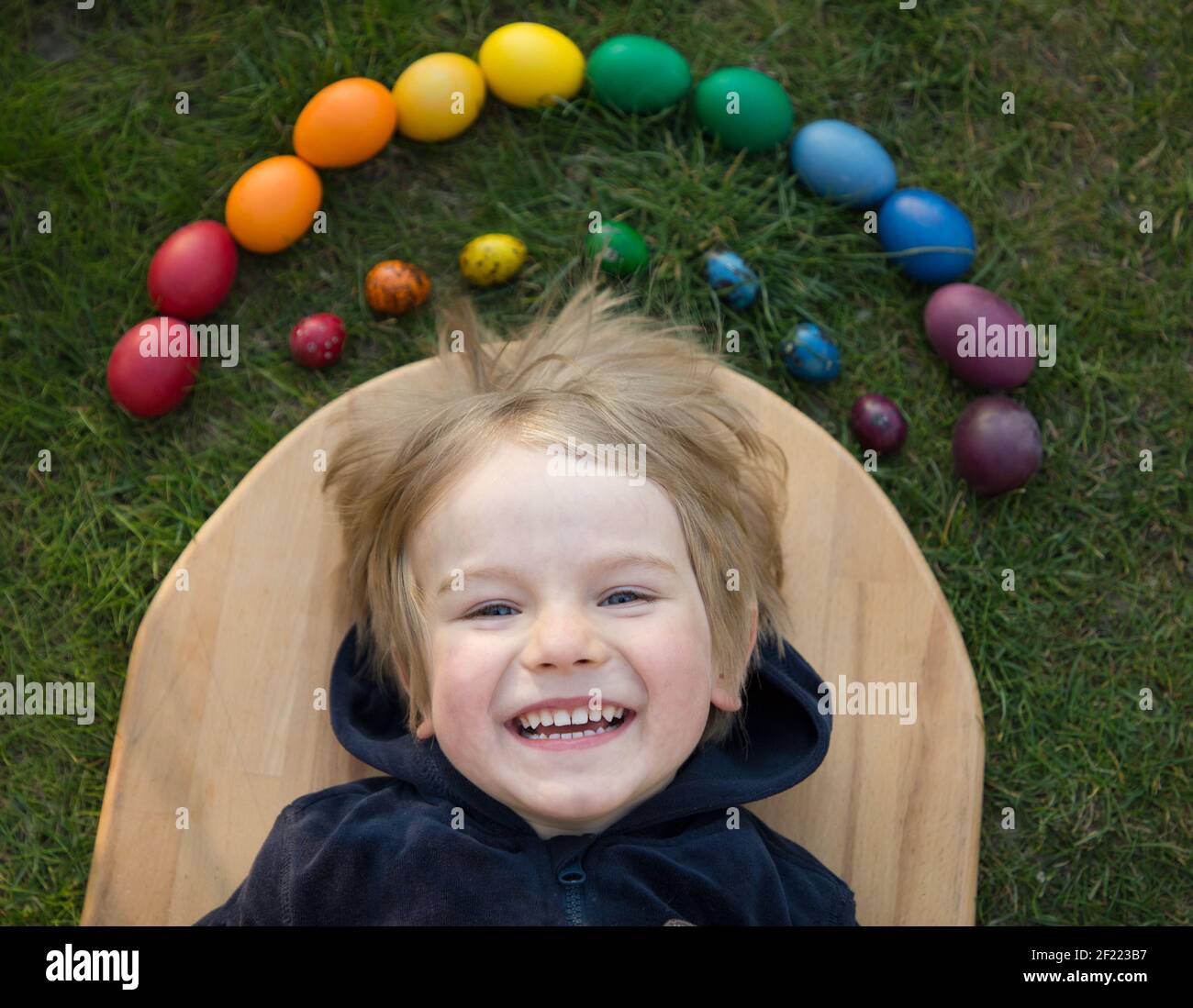 Happy toddler boy si trova vicino a pollo e uova di quaglia brillantemente dipinte in colori arcobaleno, soleggiata vacanza di primavera. Tradizioni familiari. Gioiosa giornata di luce di EA Foto Stock