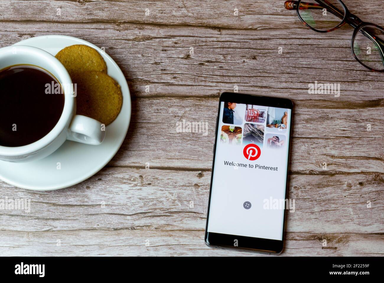 Un telefono cellulare o un telefono cellulare posato su un legno Tavolo con un'app Pinterest che apre anche un caffè e. occhiali Foto Stock
