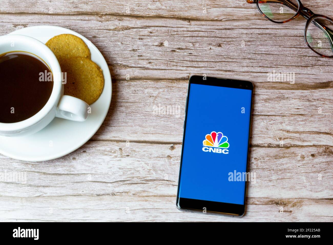 Un telefono cellulare o un telefono cellulare posato su un legno Tavolo con un'app di notizie CNBC che apre anche un caffè e bicchieri Foto Stock