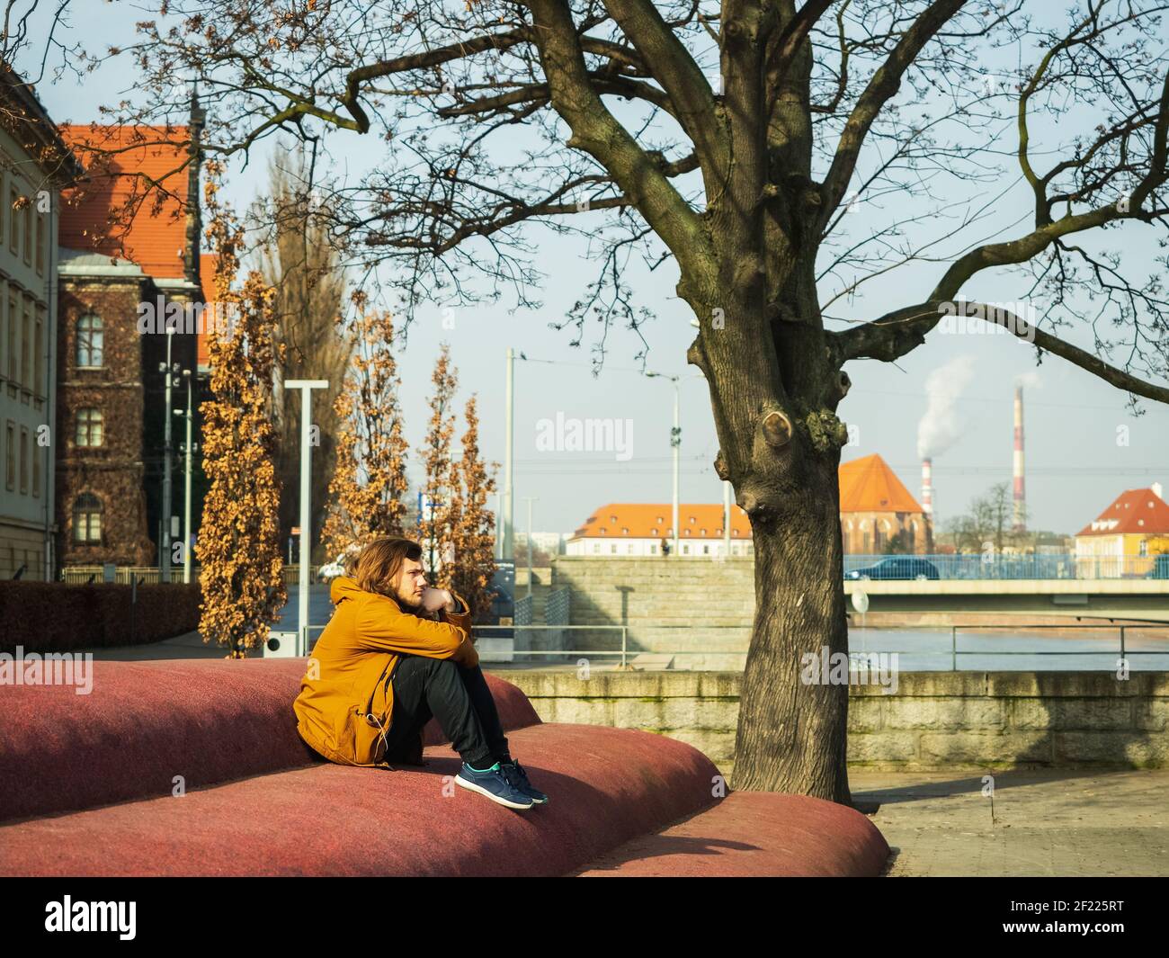 Triste giovane seduto da solo in una città, nello spazio urbano e guardando da un lato Foto Stock