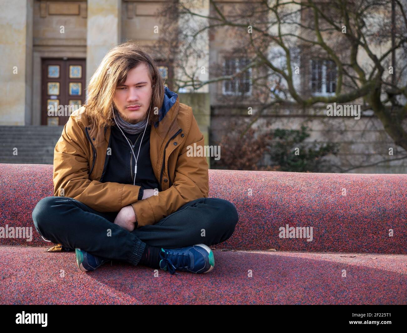Triste giovane seduto da solo in una città urbana spazio e ascoltare musica Foto Stock