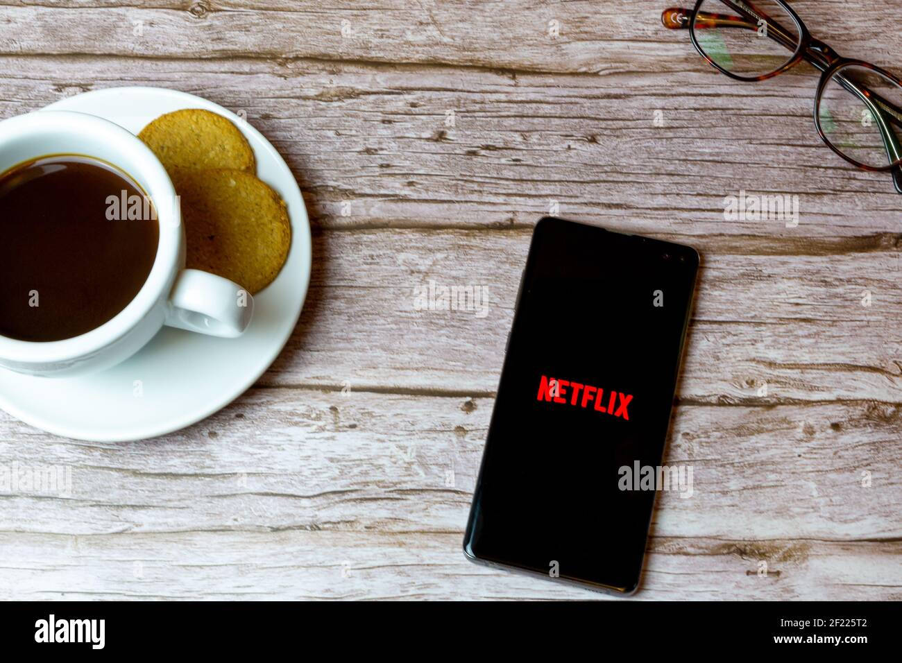 Un telefono cellulare o un telefono cellulare posato su un legno Tavolo con l'app Netflix che apre anche un caffè e. occhiali Foto Stock