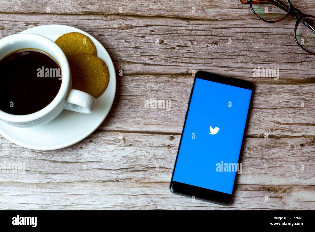 Un telefono cellulare o un telefono cellulare posato su un legno Tavolo con l'app Twitter che apre anche un caffè e. occhiali Foto Stock
