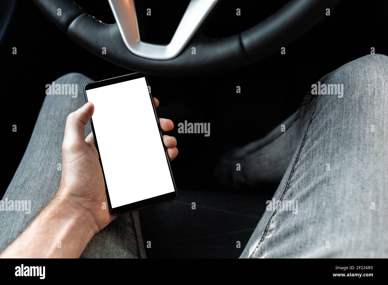 Vista interna di una nuova vettura moderna. Giovane conducente che utilizza smartphon in auto durante la guida o il parcheggio. Mockup di un telefono cellulare wi Foto Stock