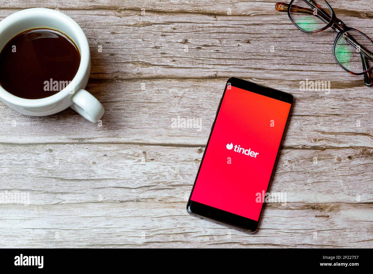 Un telefono cellulare o un telefono cellulare posto su un tavolo O scrivania con l'app di datazione Tinder aperta e una caffè accanto ad esso Foto Stock