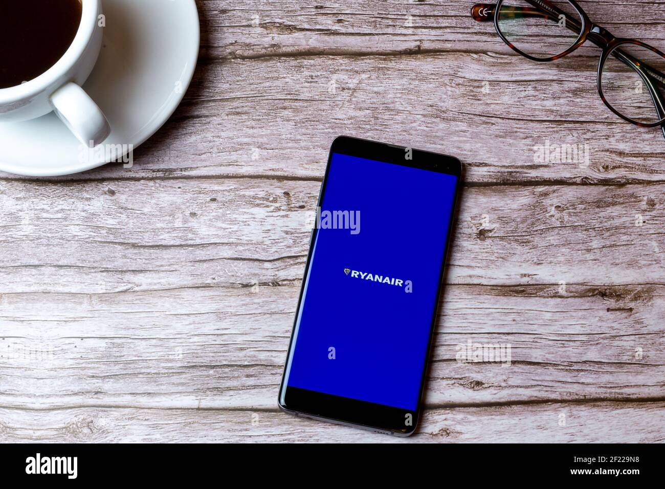 Un telefono cellulare o un telefono cellulare posato su un legno Tavolo con l'app Ryanair aperta accanto a un caffè e bicchieri Foto Stock
