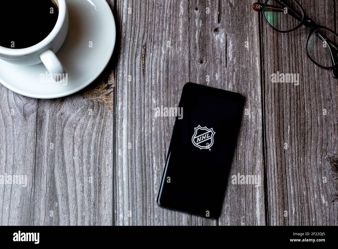 Un telefono cellulare o un telefono cellulare posato su un legno Tabella con l'app NHL Hockey aperta sulla schermata successiva ad un caffè Foto Stock