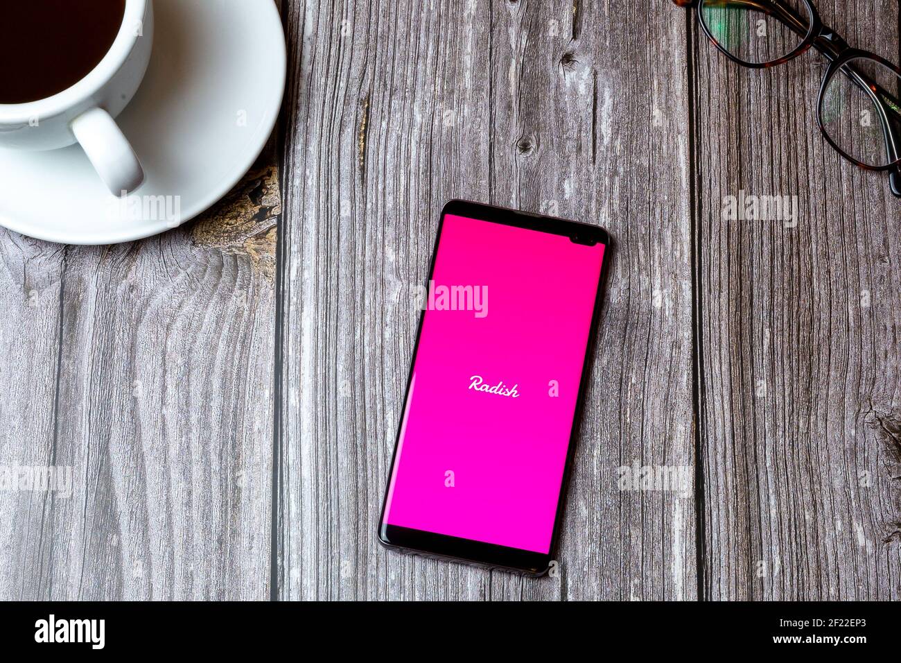 Un telefono cellulare o un telefono cellulare posato su un legno tavolo con l'app radish aperta sullo schermo accanto a. un caffè Foto Stock