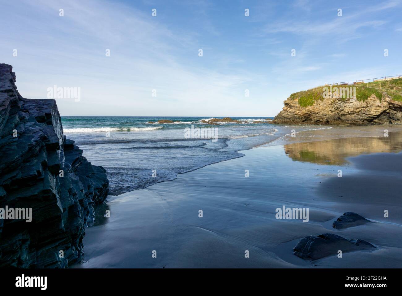 Calda serata d'oro su una spiaggia di sabbia con jagged e. scogliere frastagliate Foto Stock