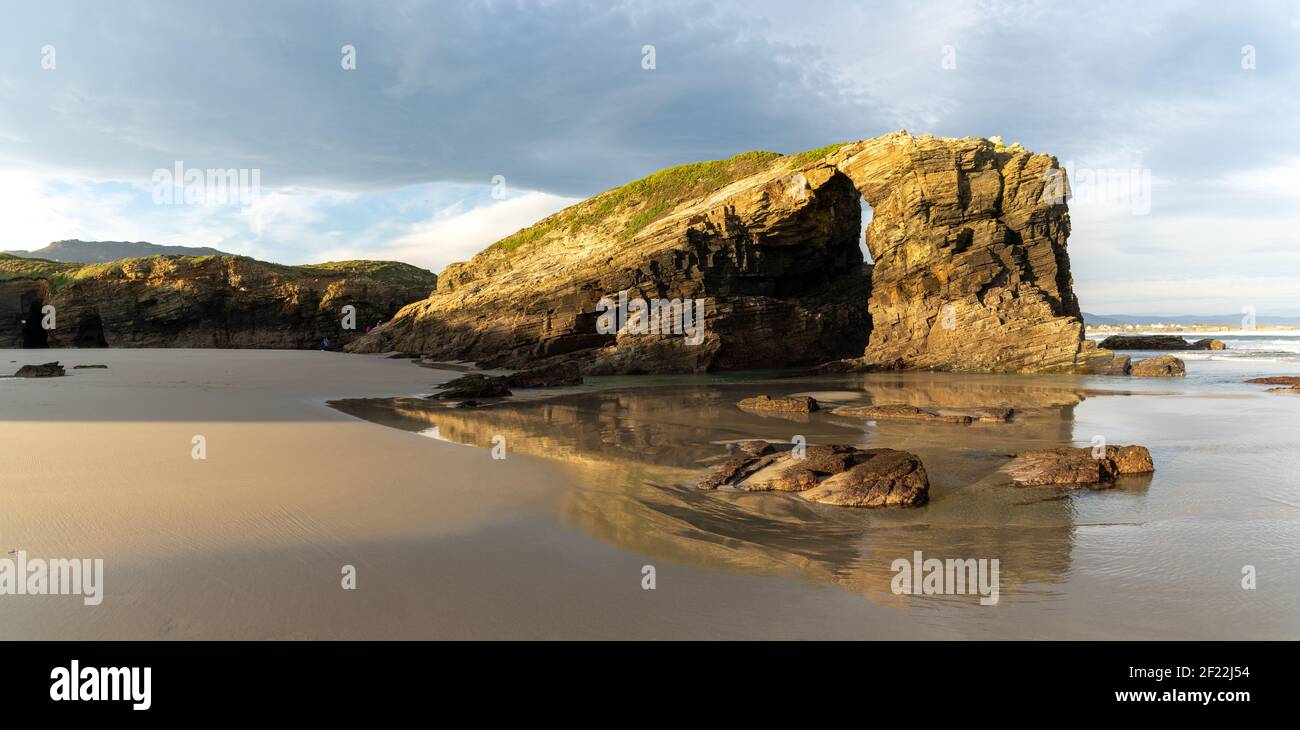 Una calda mattina dorata su una spiaggia di sabbia con frastagliata e scogliere aspre Foto Stock