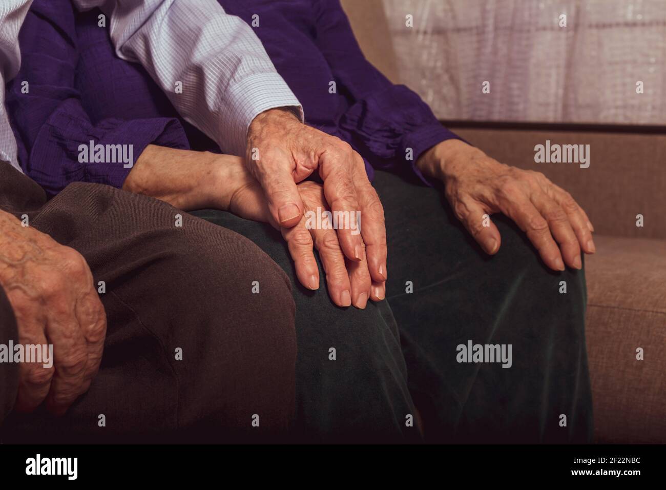 Coppie anziane che si sostengono a vicenda seduti sul divano. L'uomo anziano sta tenendo la mano della donna in casa di cura. Amore alla morte. Le mani di una persona molto anziano. Foto Stock