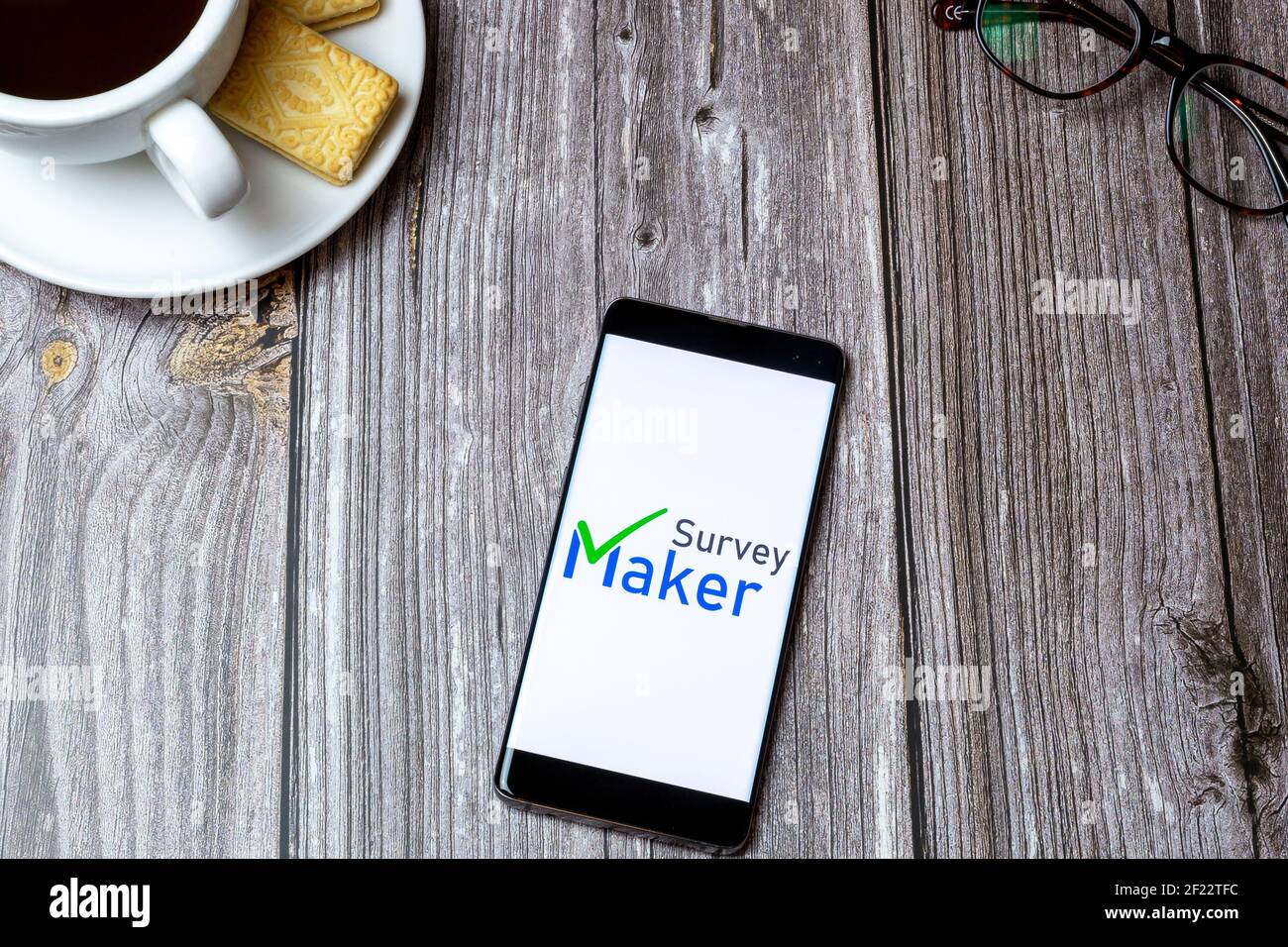 Un telefono cellulare o cellulare su un tavolo di legno Con l'app Survey Maker aperta accanto a un caffè e bicchieri Foto Stock