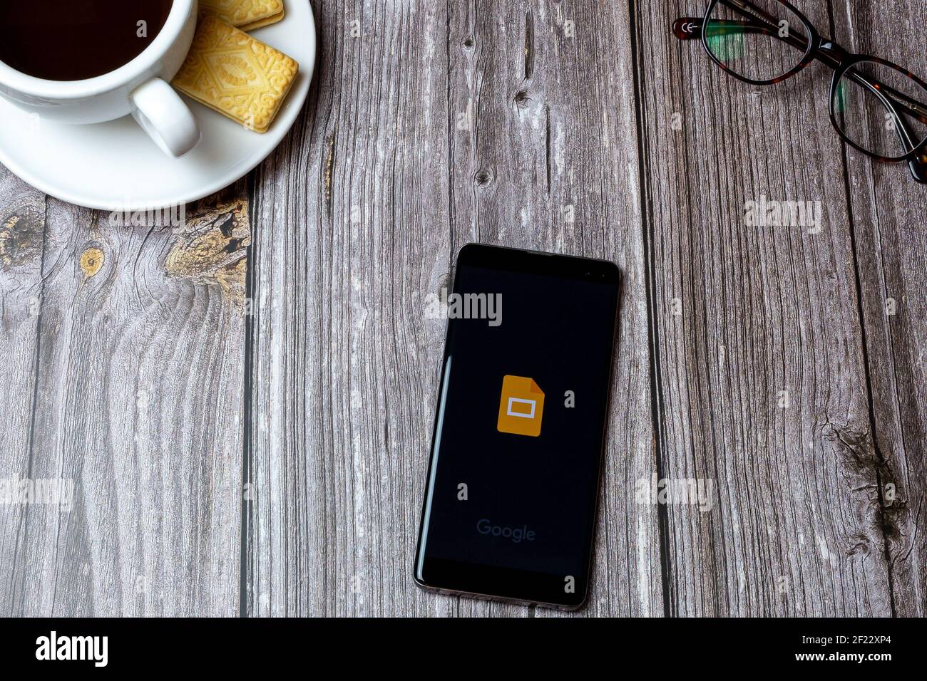 Un telefono cellulare o cellulare su un tavolo di legno Con l'app Google Slides aperta accanto a un caffè e bicchieri Foto Stock
