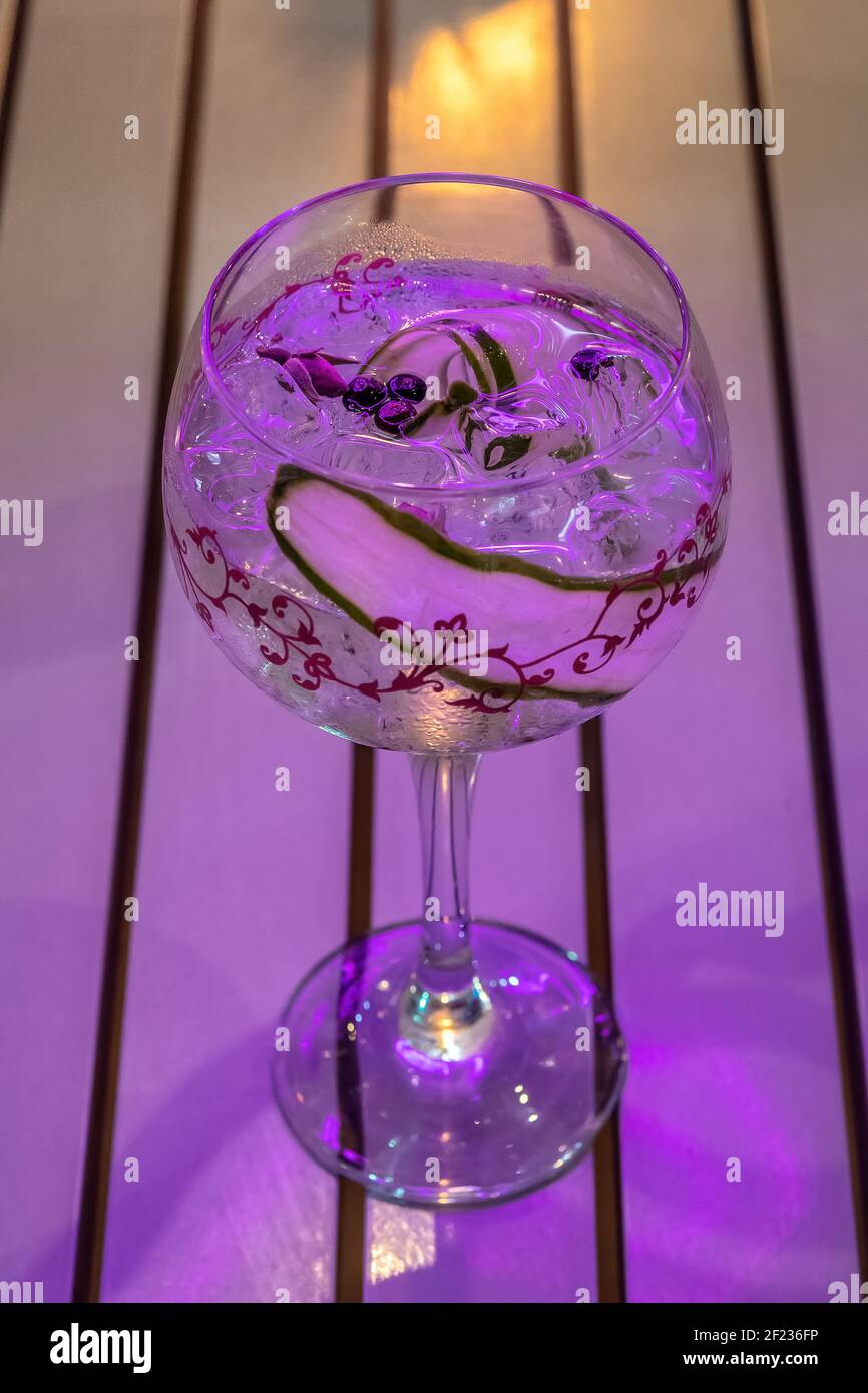 Cocktail fresco con cetriolo in un bicchiere di vino con luce al neon. Festa d'estate di fondo. Foto Stock