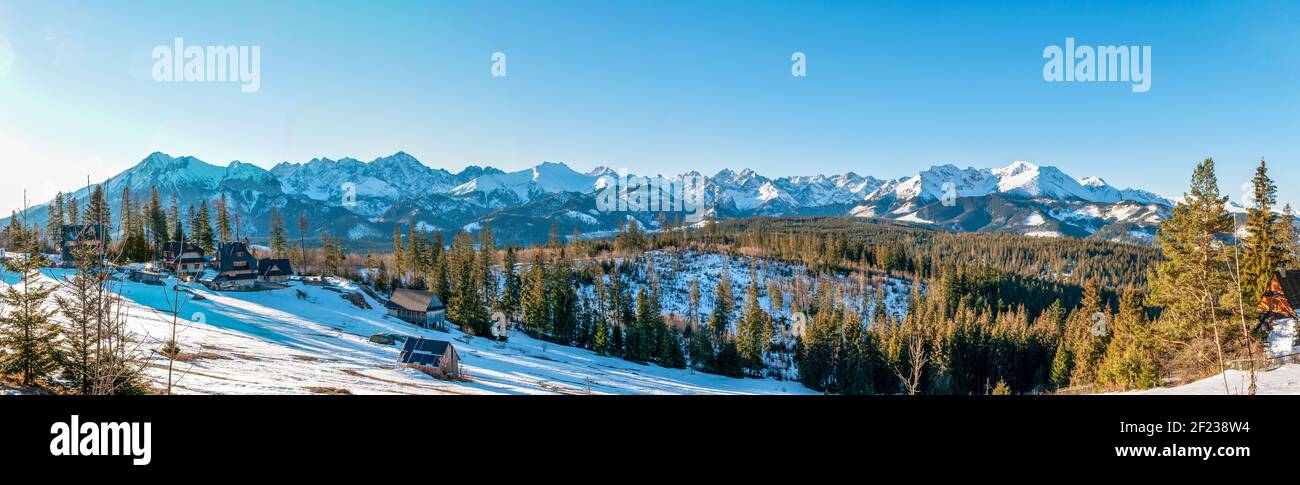 Ampio panorama invernale dei Monti Tatra all'alba con un villaggio, case e foresta Foto Stock