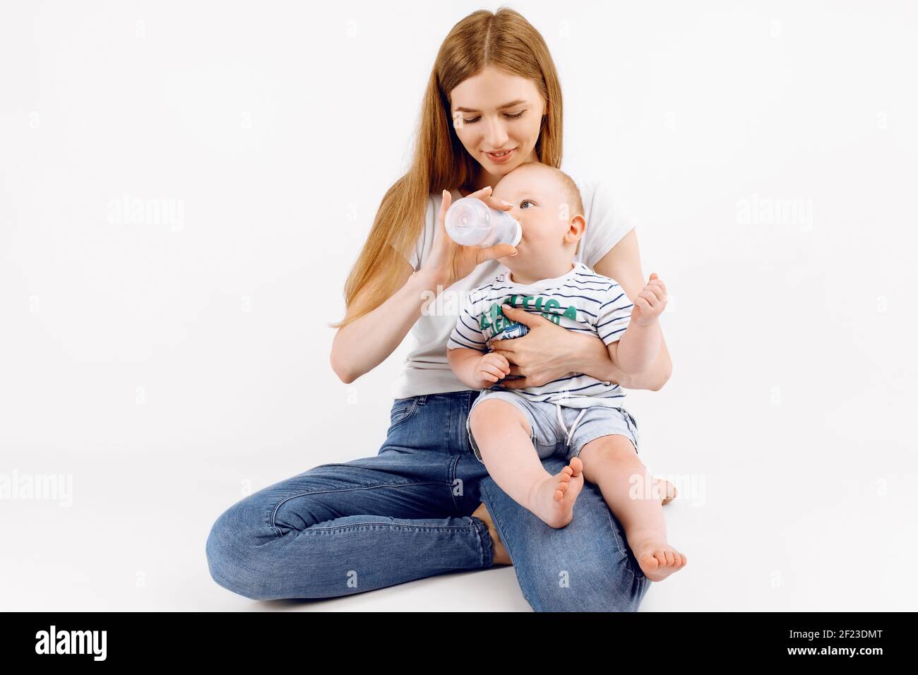 Felice madre sorridente che alimenta il suo bambino da un biberon, su sfondo bianco isolato Foto Stock