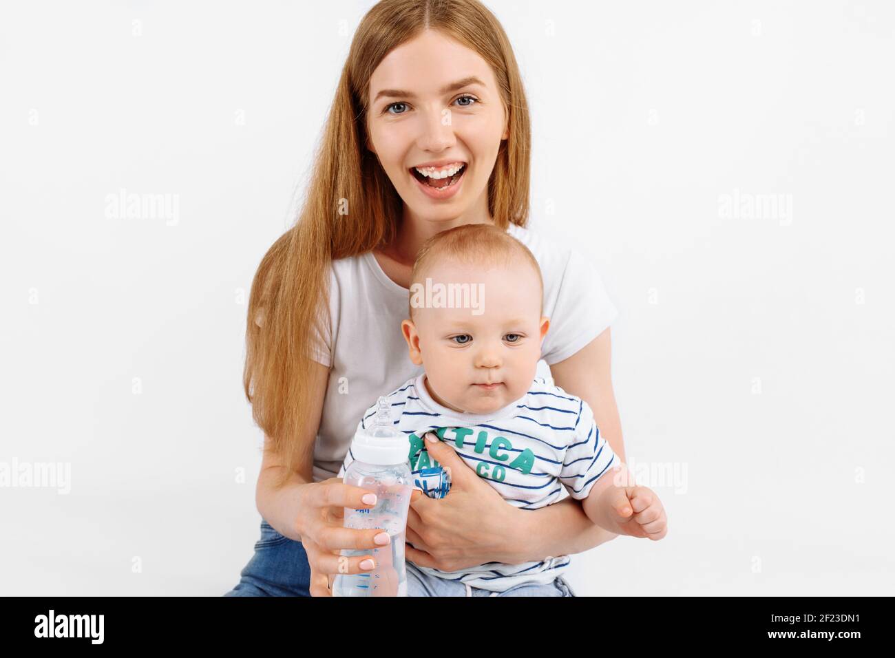 Felice madre sorridente che alimenta il suo bambino da un biberon, su sfondo bianco isolato Foto Stock