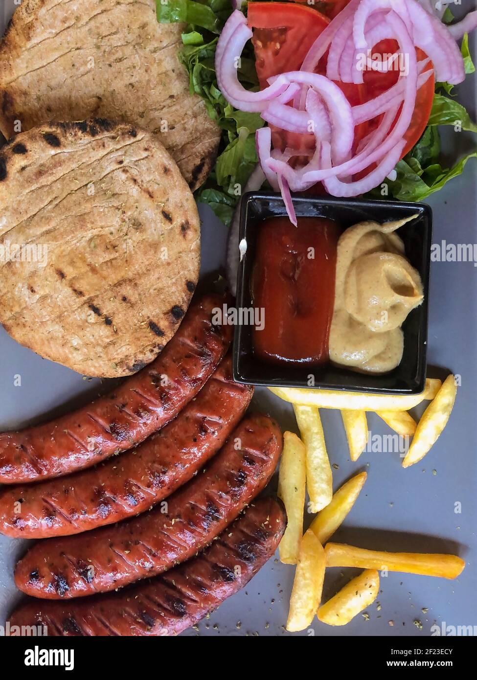 Piatto di salsiccia alla griglia con patatine fritte e salse, pane e verdure. Foto Stock