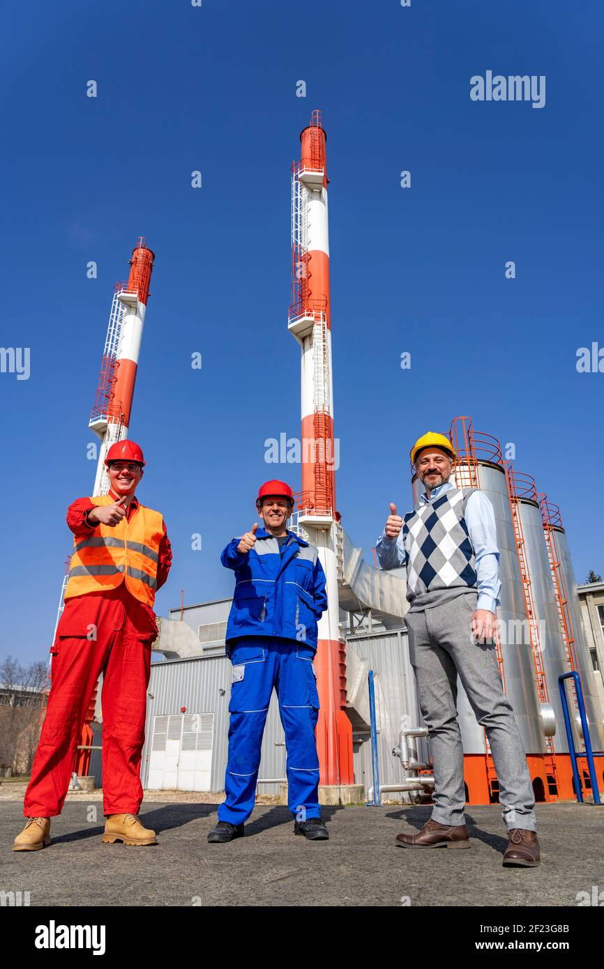 Due lavoratori in dispositivi di protezione individuale incontro con un uomo d'affari. Centrale elettrica di riscaldamento urbano. Concetto di lavoro di squadra. Foto Stock