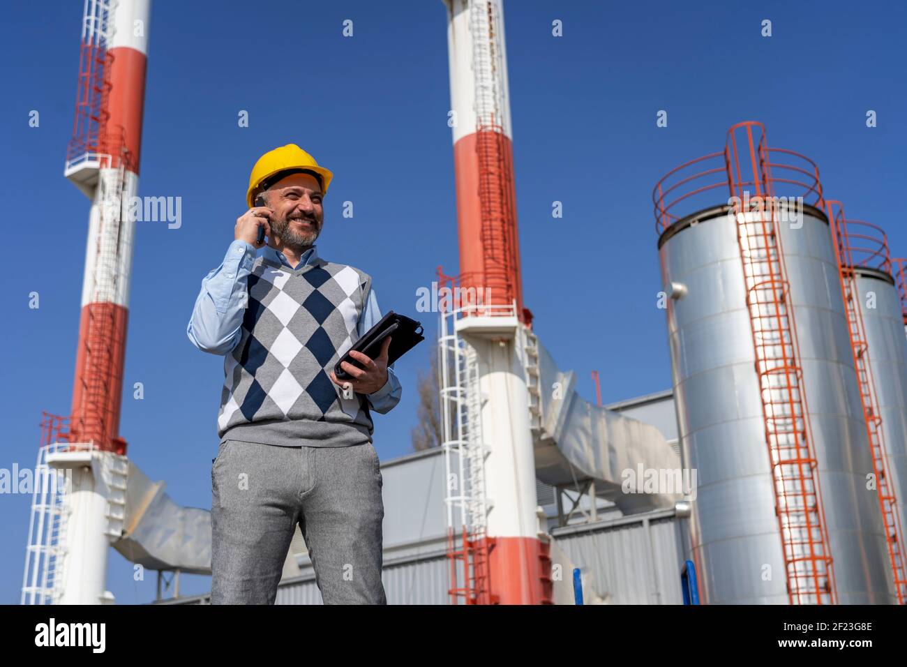 Ritratto di Smiling Manager con telefono cellulare e tablet digitale nella centrale di riscaldamento distrettuale. Foto Stock