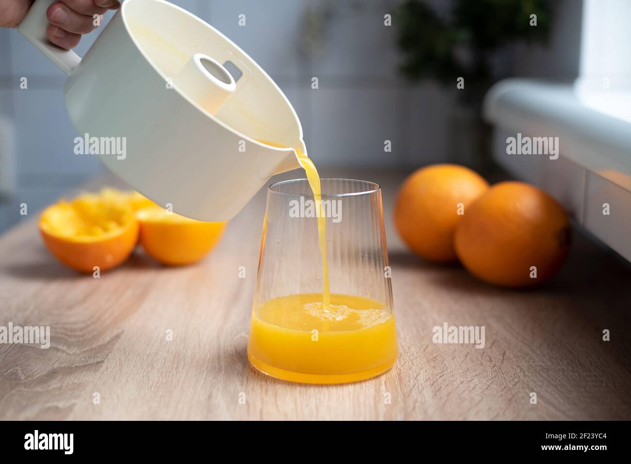 Succo d'arancia fresco che si versa da una centrifuga in un bicchiere con arance schiacciate, in cucina, primo piano Foto Stock