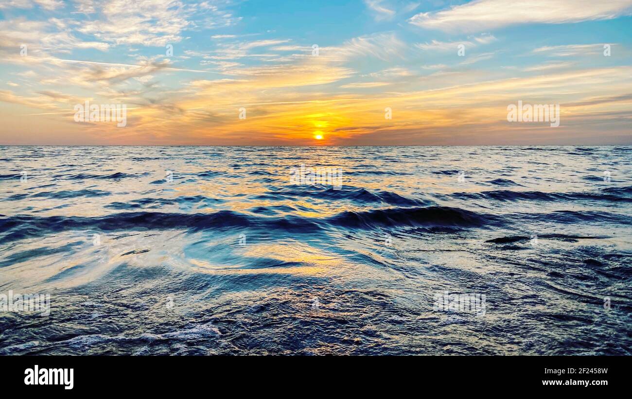 Un mare irrequieto con cielo arancione tramonto e sole attraverso le nuvole sopra. Meditazione oceano e cielo sfondo. Tranquillo paesaggio marino. Orizzonte sopra l'acqua. WA Foto Stock