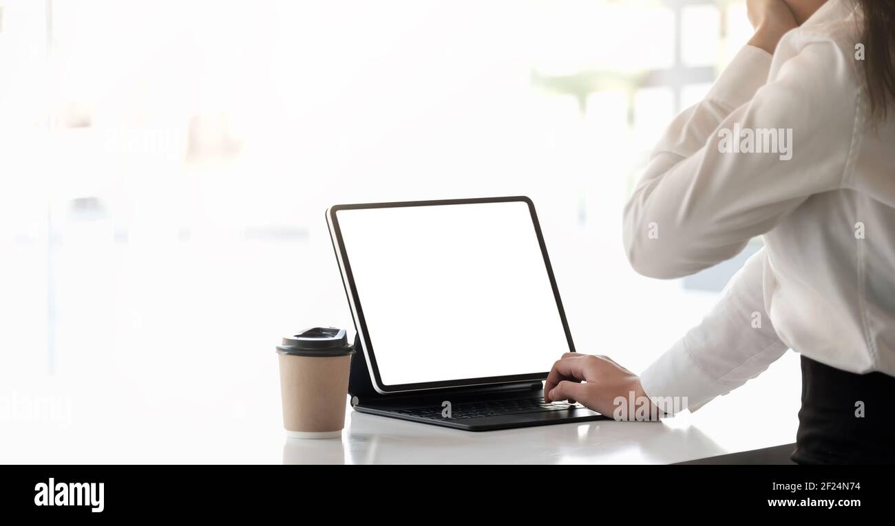 Giovane donna assonnata vestita di camicia seduta sul suo posto di lavoro digitazione dello schermo vuoto del tablet intelligente Foto Stock