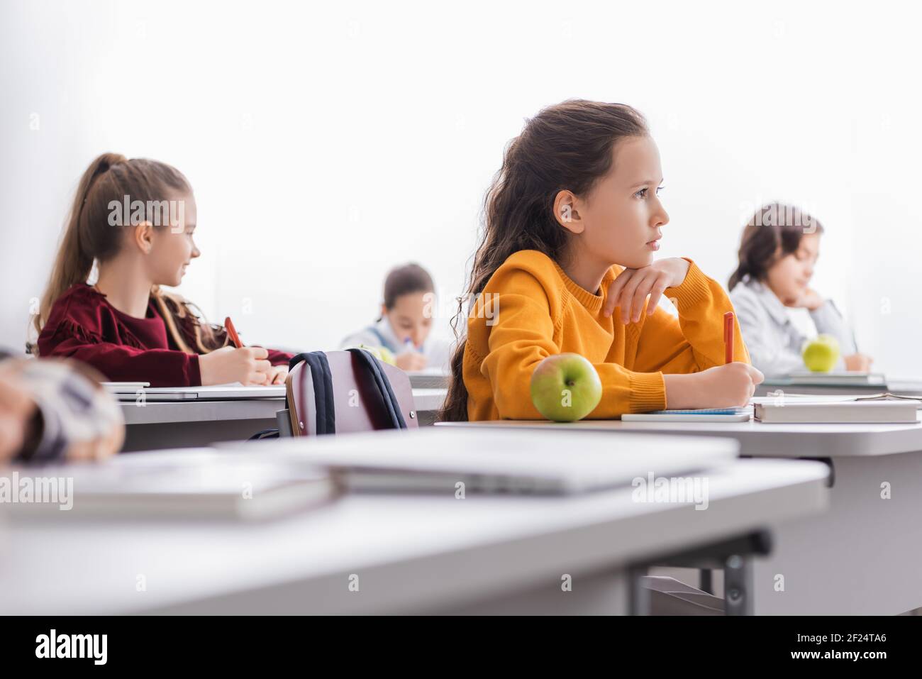 Schoolchild che tiene la penna vicino al notebook, libro e mela sulla scrivania Foto Stock