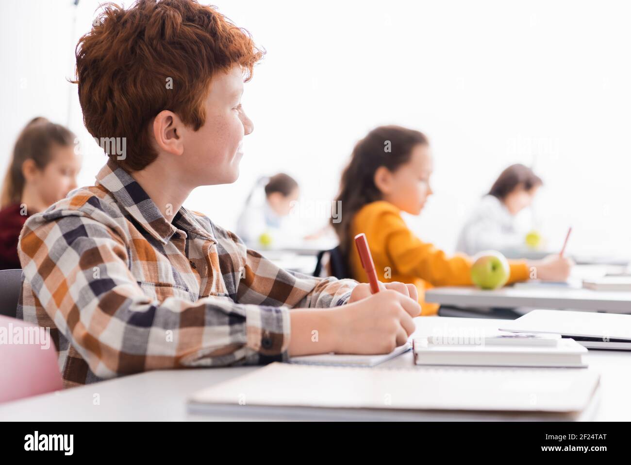 Scolaro che scrive sul notebook vicino al portatile su primo piano sfocato in in aula Foto Stock