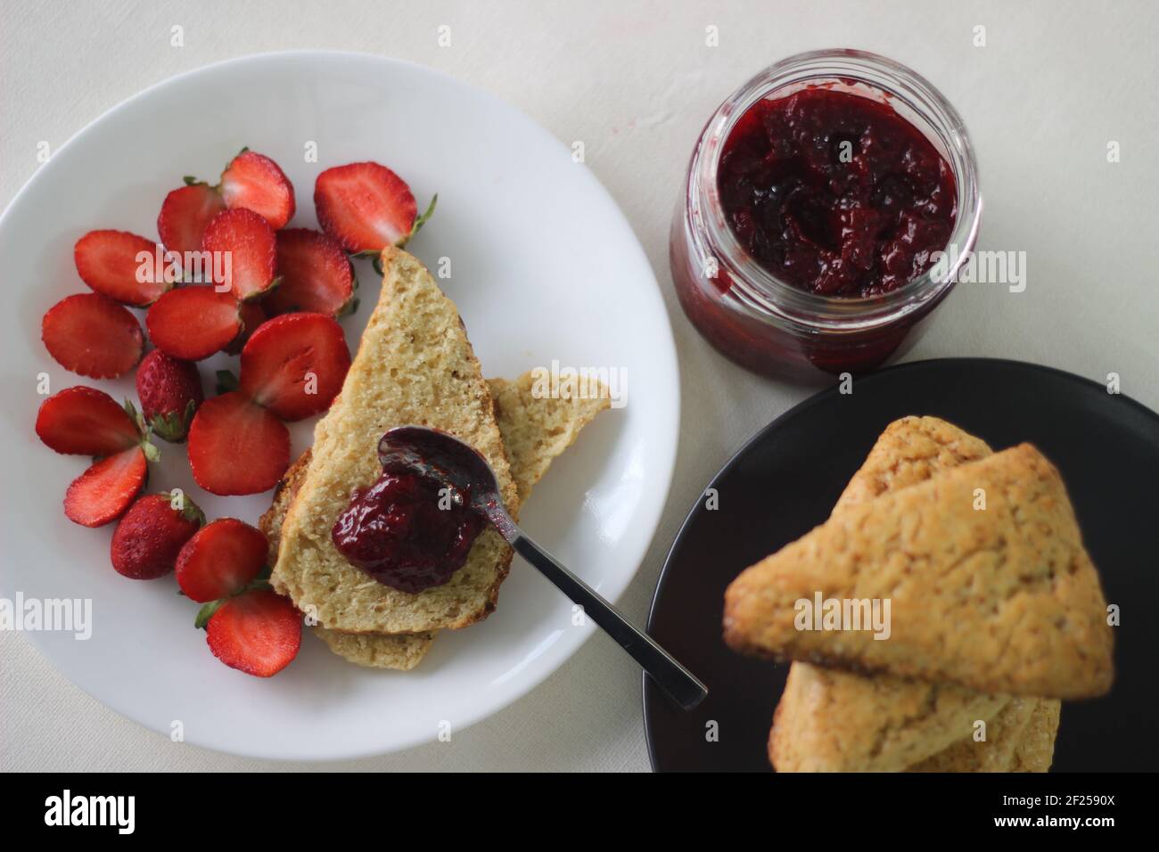 Focaccine di latticello dolce appena cotte in casa servite con marmellata di fragole fatte in casa e fragole tagliate fresche. Scatto su sfondo bianco Foto Stock