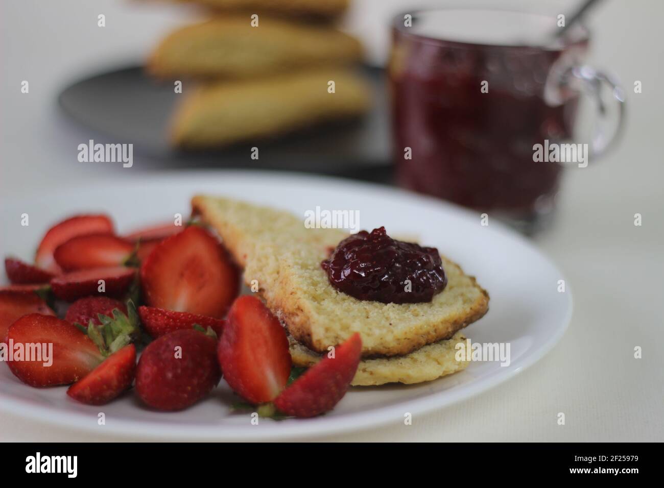 Focaccine di latticello dolce appena cotte in casa servite con marmellata di fragole fatte in casa e fragole tagliate fresche. Scatto su sfondo bianco Foto Stock