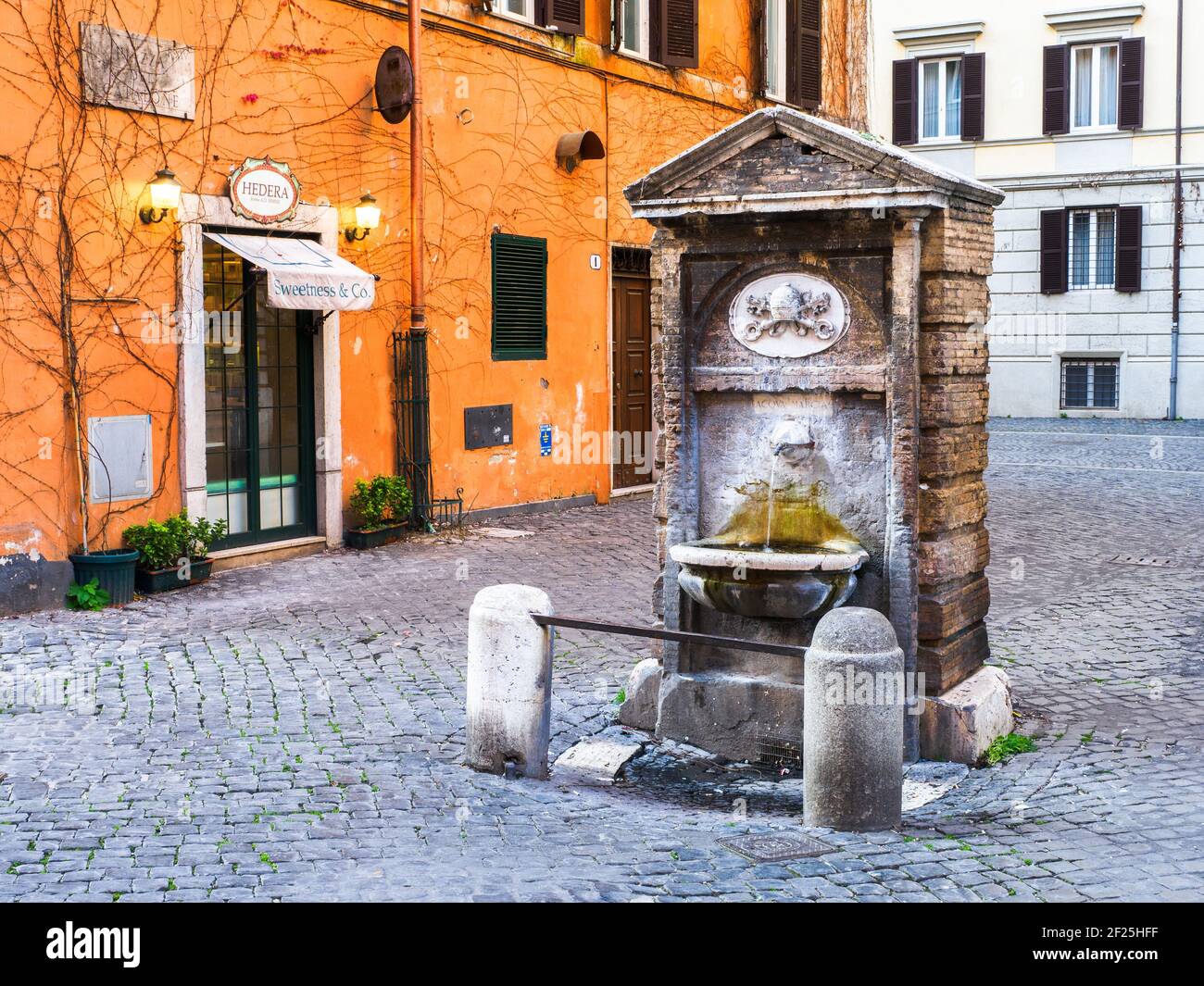 La fontana del rione Borgo è protetta da due colonnine collegate da una barretta di ferro, costituita da una semplice edicola rettangolare in travertino, che si inclina in alto e si appoggia contro una costruzione in mattoni. L'arco superiore ha uno stemma papale - Roma, Italia Foto Stock