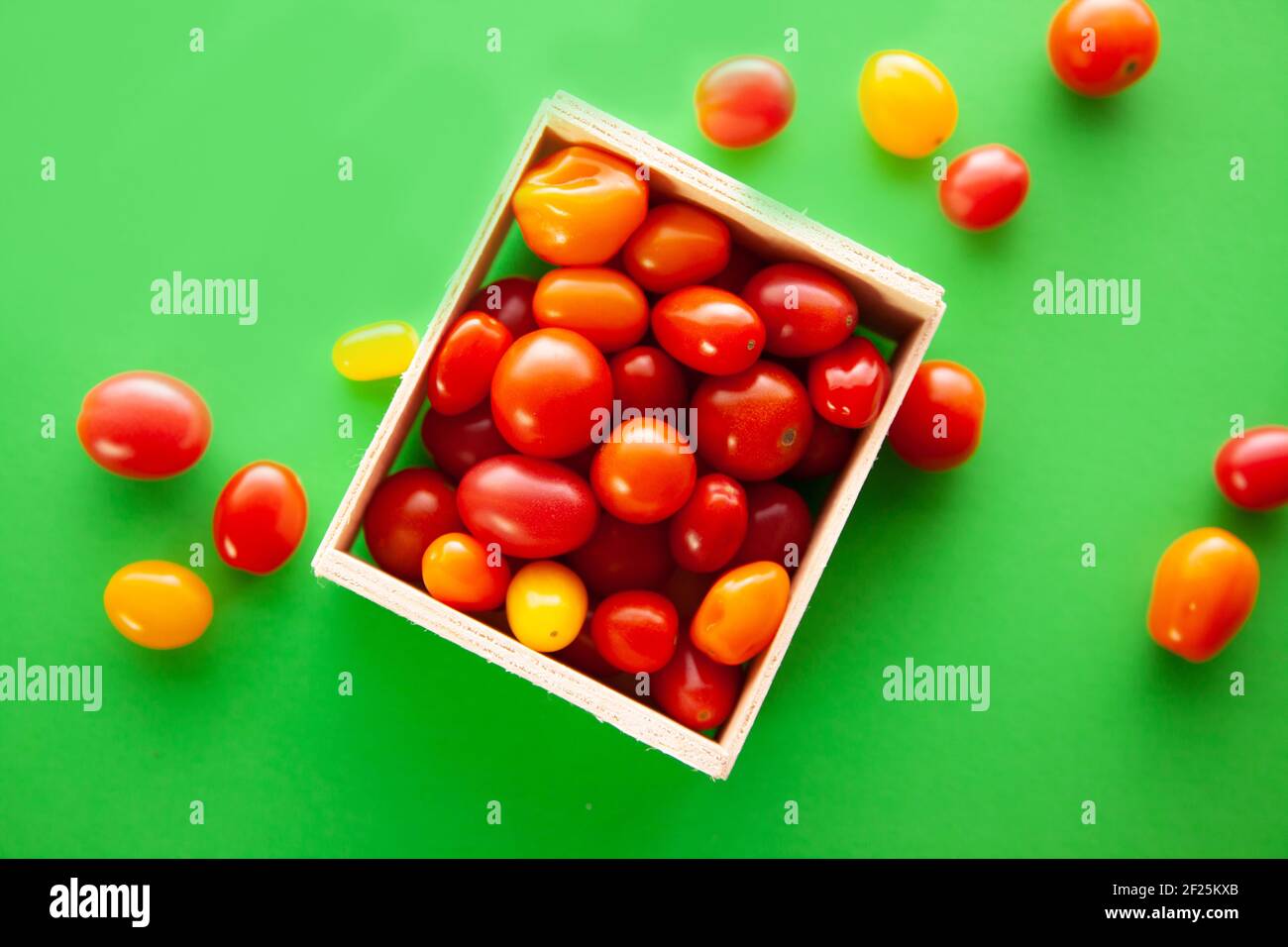 Scatola di legno con pomodori ciliegini freschi. Pomodori ciliegini rossi, arancioni e gialli su sfondo verde Foto Stock