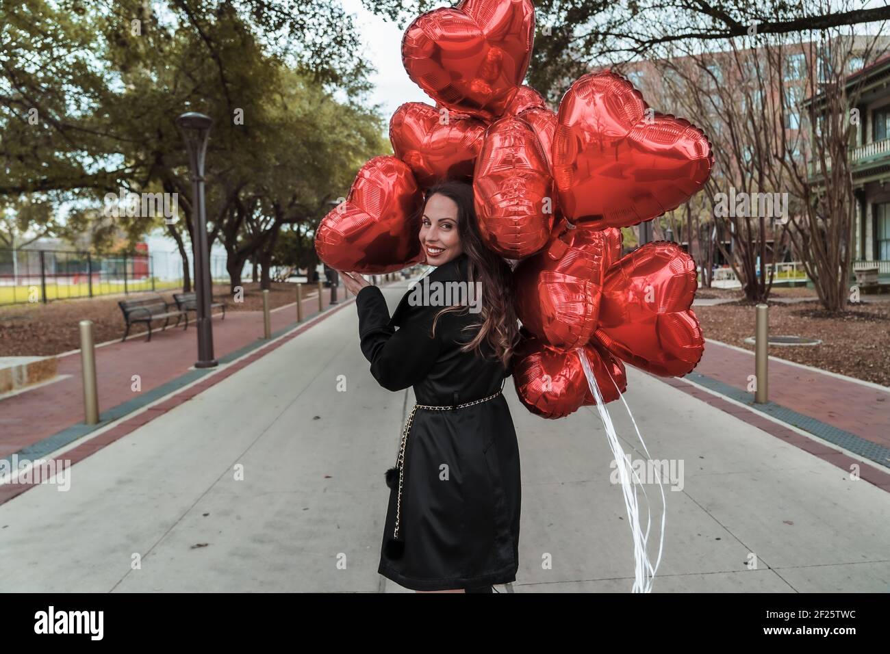 La splendida Brunette ispanica celebra il giorno di San Valentino con una dozzina Palloncini con cuore rosso Foto Stock